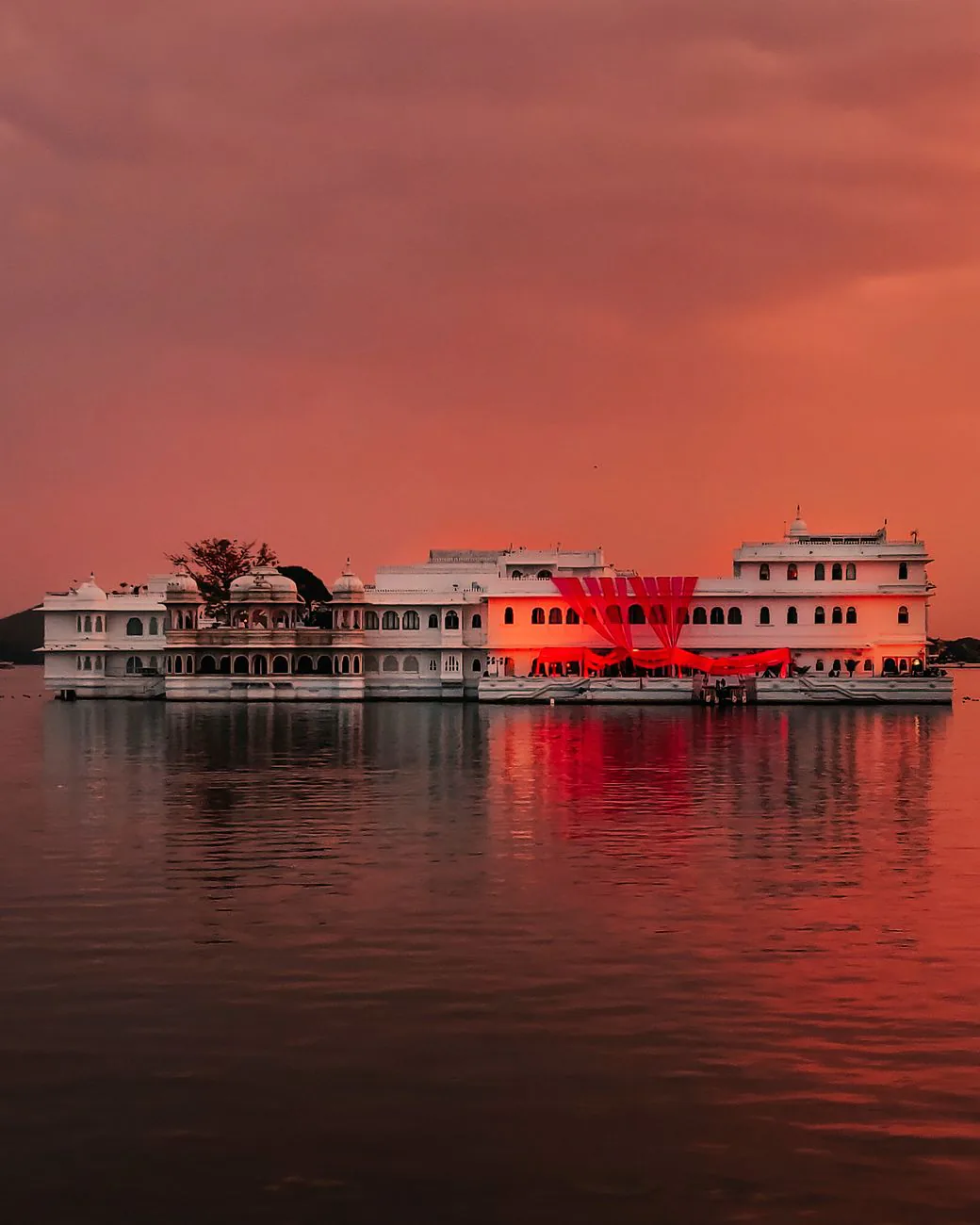 The Lake Palace of Udaipur glowing under a vibrant sunset sky, reflected on the calm waters of Lake Pichola, Rajasthan