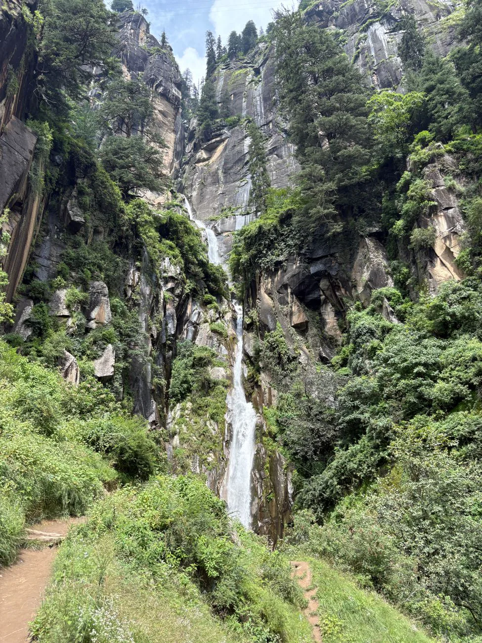 Waterfall cascading through green mountain forest near Manali