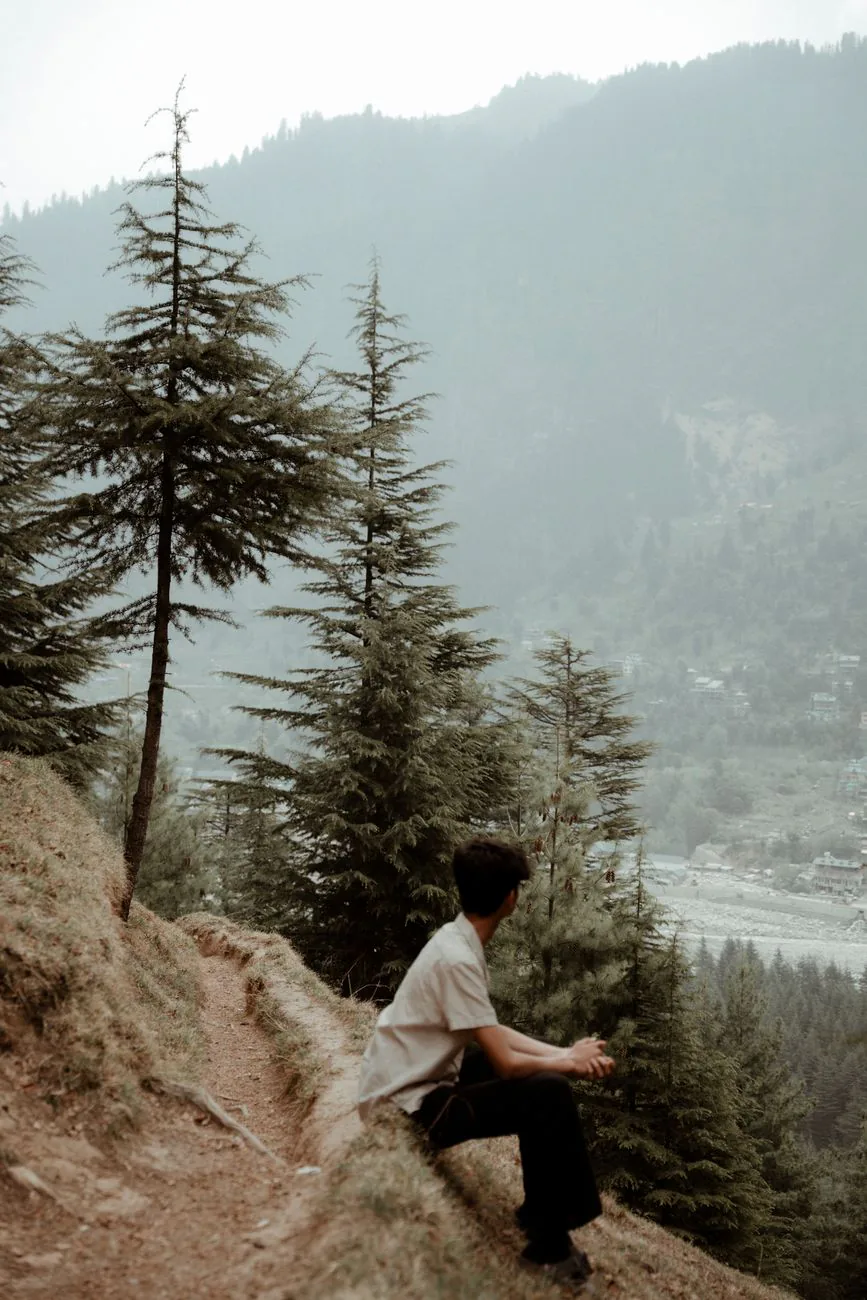 A traveler resting on a quiet mountain trail surrounded by misty peaks