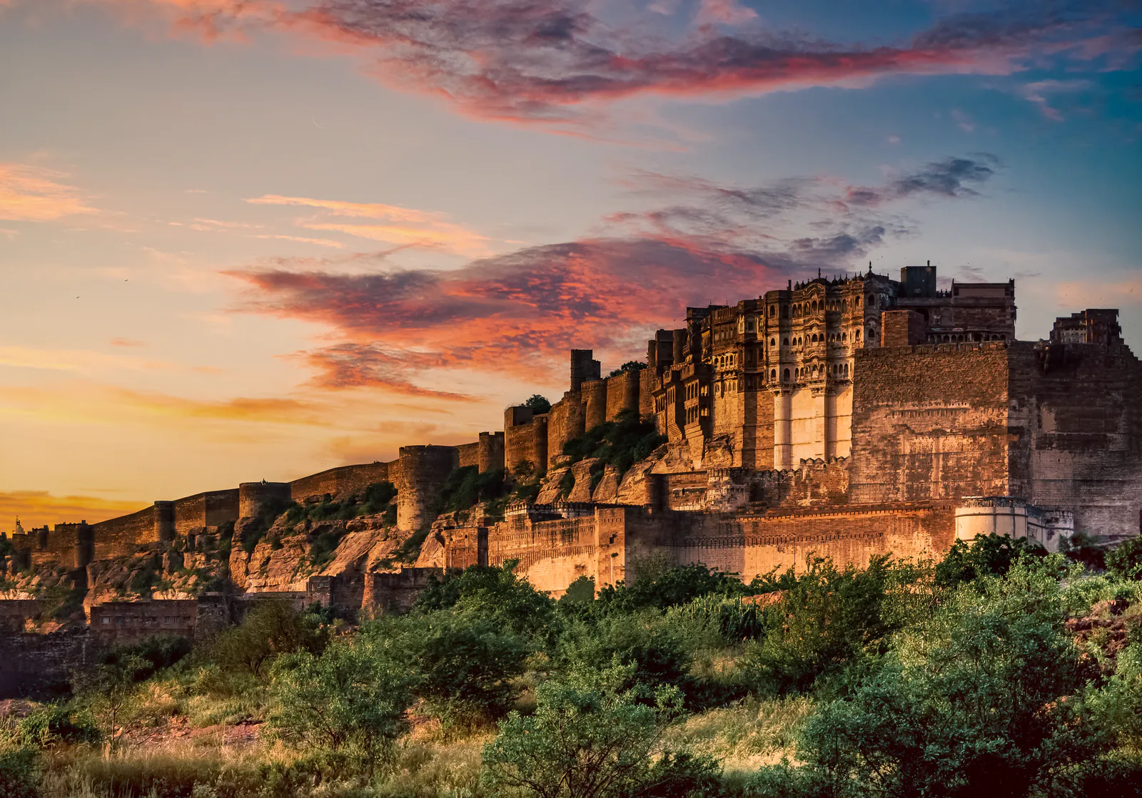Mehrangarh Fort towering above Jodhpur's blue rooftops under a vibrant sunset sky in Rajasthan
