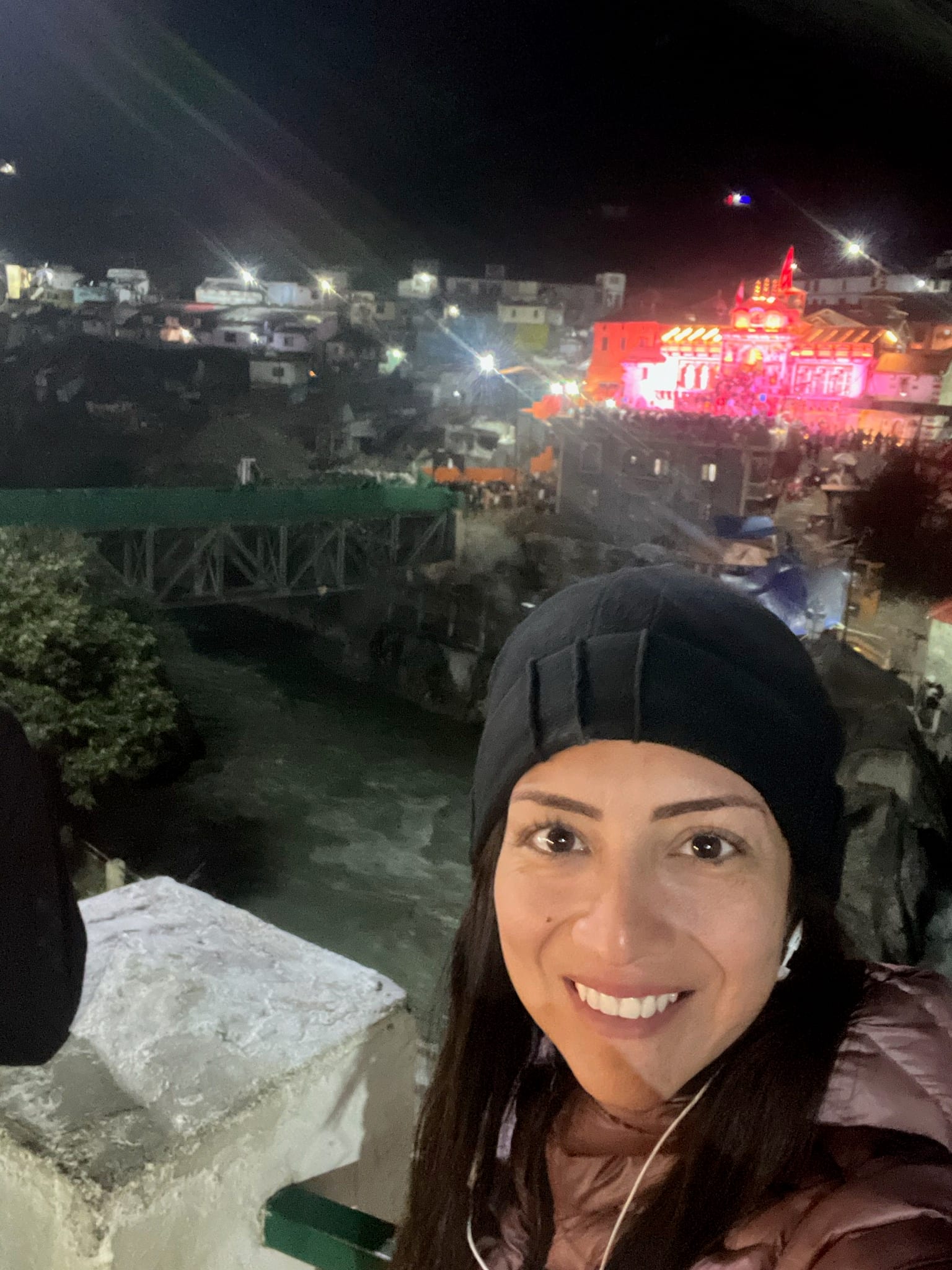 Night selfie wearing a black hat in front of the illuminated Badrinath Temple.