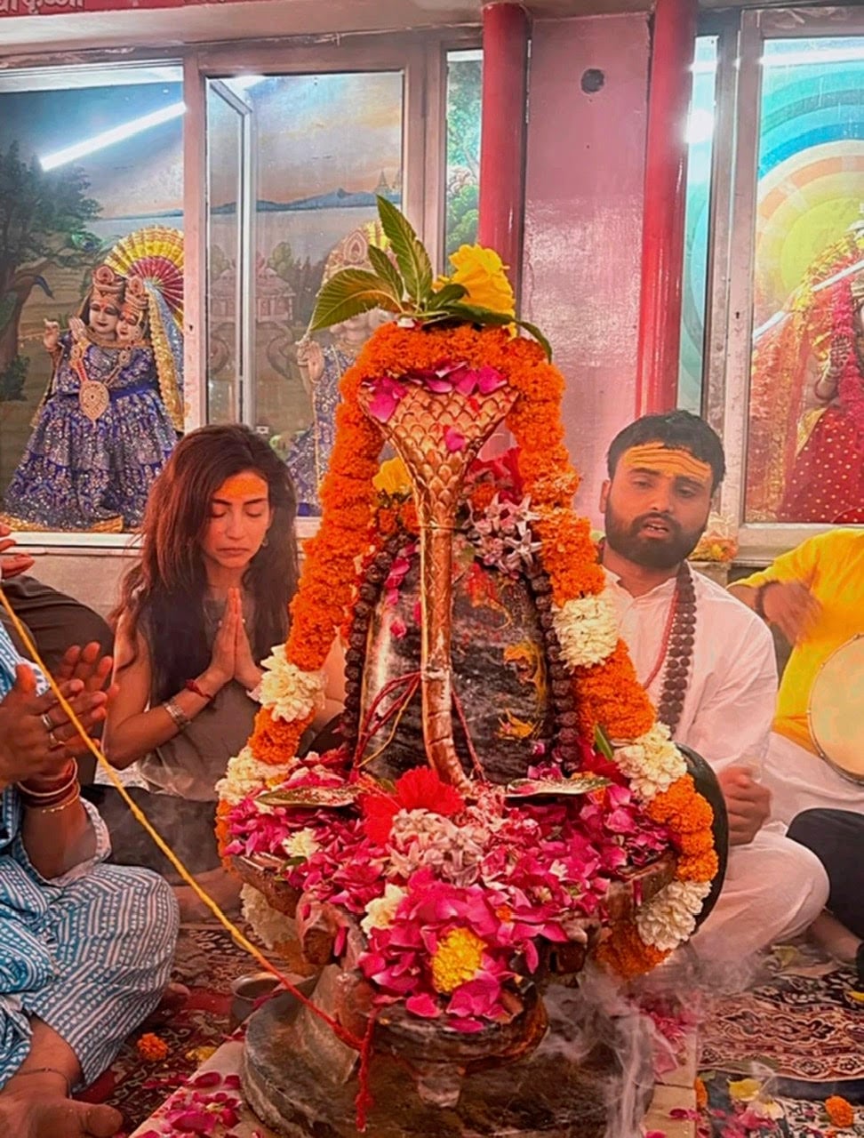 Traveler with hands in prayer beside a flower-covered sacred altar during a temple ceremony in India
